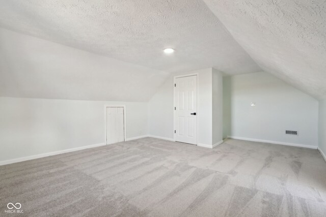 bonus room featuring a textured ceiling, carpet, baseboards, and vaulted ceiling