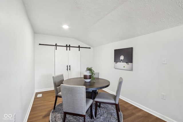 dining area with baseboards, lofted ceiling, dark wood-style flooring, a textured ceiling, and a barn door