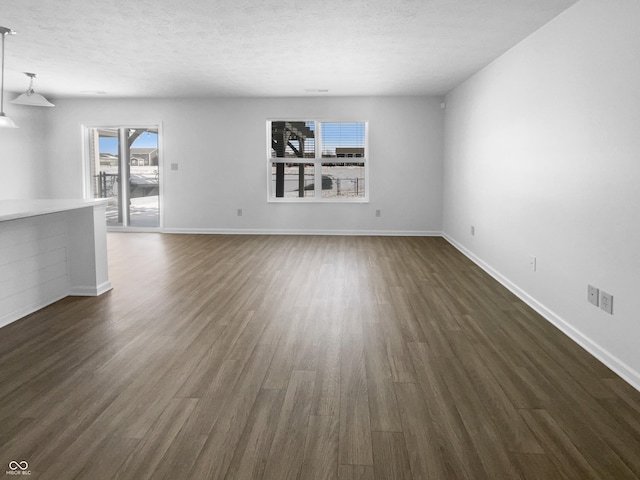 unfurnished living room featuring baseboards, a textured ceiling, and dark wood-style floors