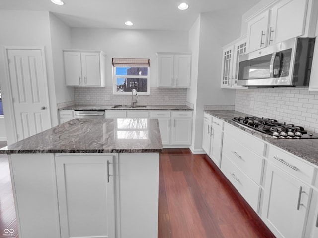 kitchen featuring dark wood finished floors, dark stone countertops, stainless steel appliances, white cabinetry, and a sink