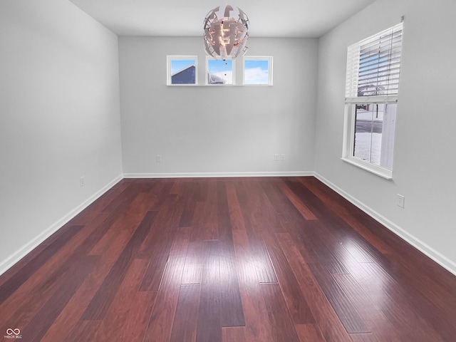 unfurnished room with a chandelier, baseboards, and hardwood / wood-style floors