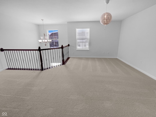 empty room featuring a chandelier, baseboards, and carpet