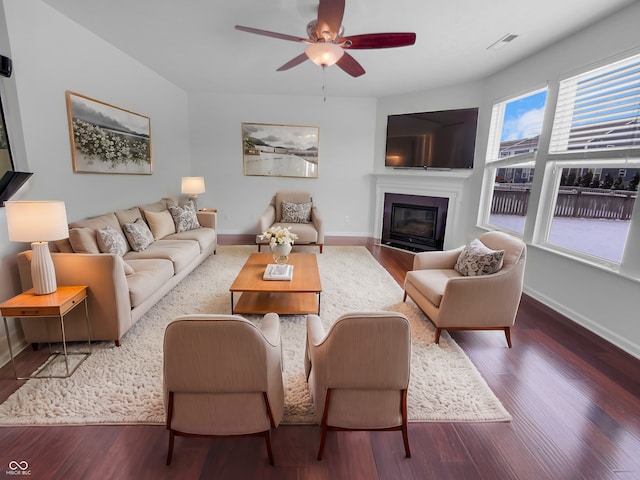 living room with a ceiling fan, visible vents, wood finished floors, baseboards, and a fireplace with flush hearth