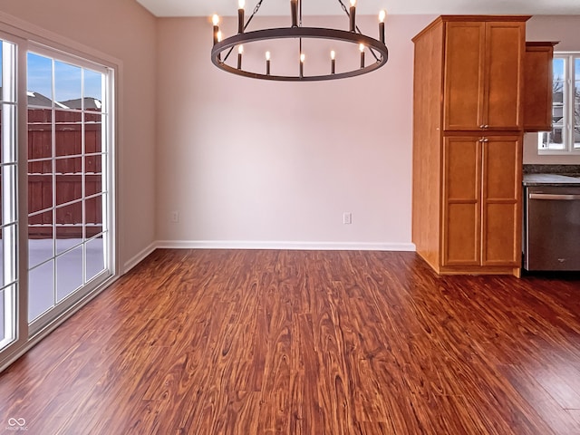 unfurnished dining area featuring a chandelier, a healthy amount of sunlight, baseboards, and dark wood-style flooring