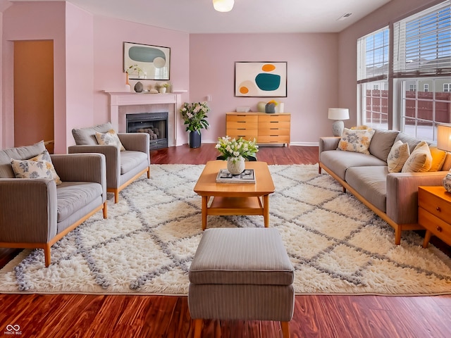 living area featuring a tiled fireplace, baseboards, and wood finished floors