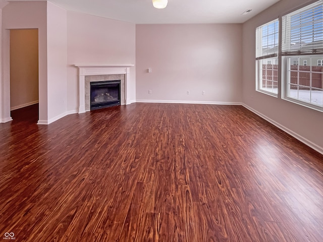 unfurnished living room featuring a tile fireplace, baseboards, and dark wood-style flooring