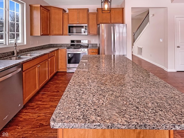 kitchen with a sink, a kitchen island, stainless steel appliances, dark stone counters, and dark wood-style flooring