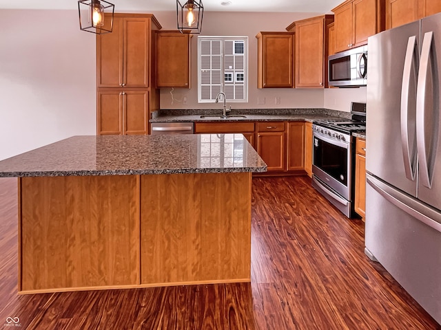 kitchen with a center island, dark wood finished floors, dark stone counters, appliances with stainless steel finishes, and a sink