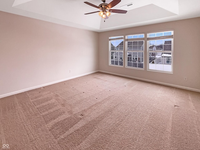 carpeted spare room featuring visible vents, ceiling fan, baseboards, and a tray ceiling