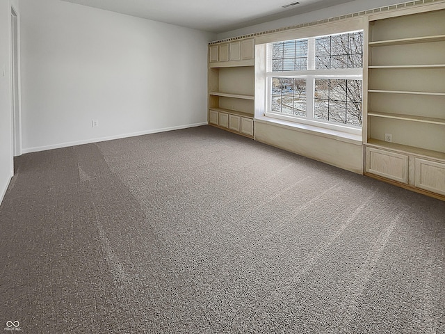 empty room featuring carpet flooring, visible vents, baseboards, and built in features