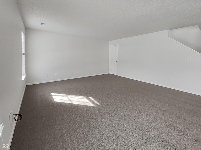 spare room featuring a textured ceiling, baseboards, and dark colored carpet