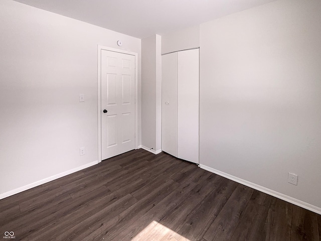 unfurnished bedroom featuring dark wood finished floors, baseboards, and a closet