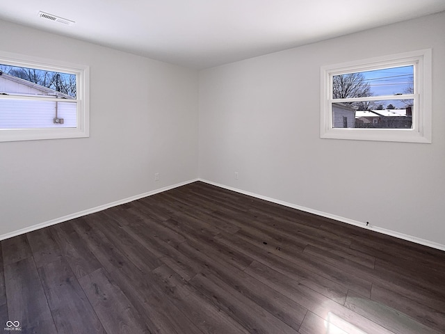 unfurnished room featuring dark wood-style floors, visible vents, and baseboards