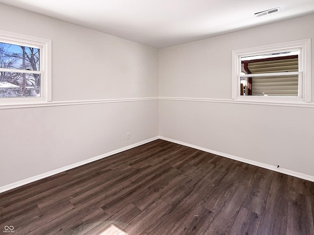 unfurnished room with dark wood-style floors, visible vents, and baseboards