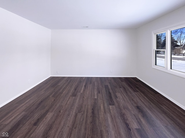 empty room featuring dark wood finished floors, visible vents, and baseboards