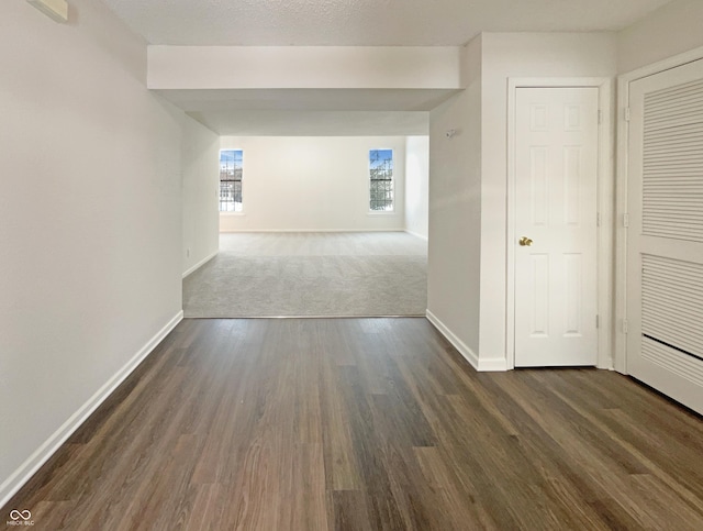 corridor featuring dark wood-type flooring and baseboards