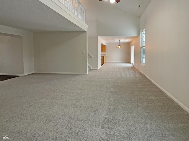 unfurnished living room featuring baseboards, stairway, carpet flooring, high vaulted ceiling, and a ceiling fan