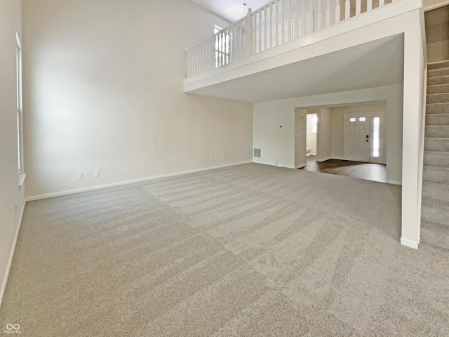 unfurnished living room featuring visible vents, baseboards, stairs, carpet floors, and a high ceiling