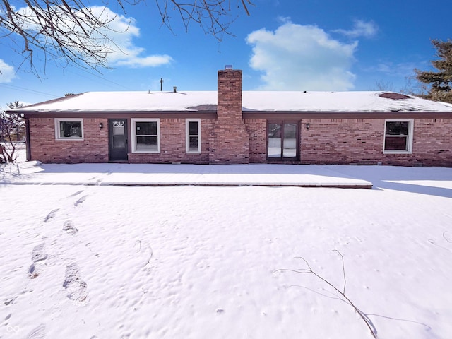 snow covered rear of property featuring brick siding and a chimney