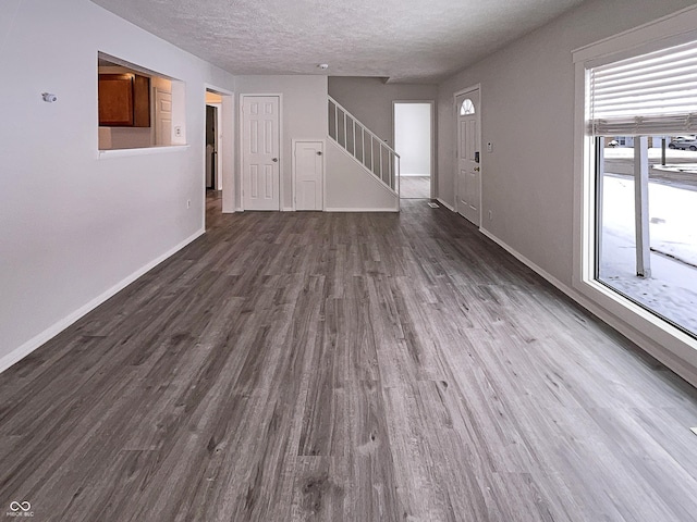 unfurnished living room featuring baseboards, dark wood-type flooring, stairs, and a textured ceiling