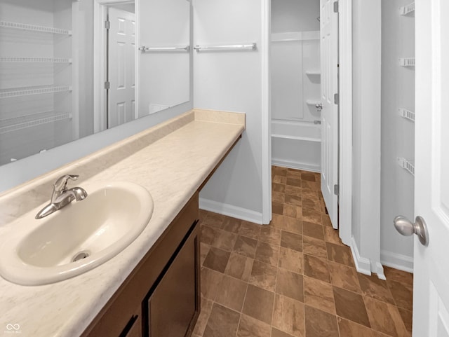 full bath featuring vanity, stone finish flooring, and baseboards