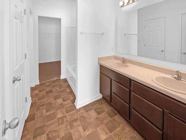 bathroom featuring double vanity, stone finish flooring, baseboards, and a sink