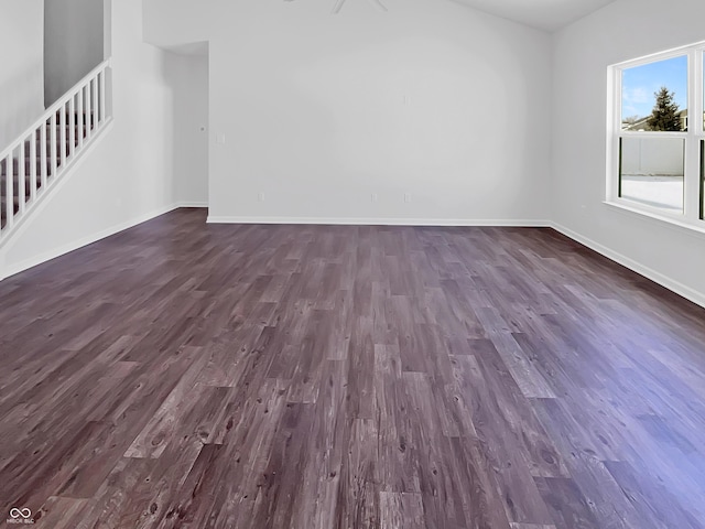 unfurnished living room featuring baseboards, dark wood finished floors, and stairs