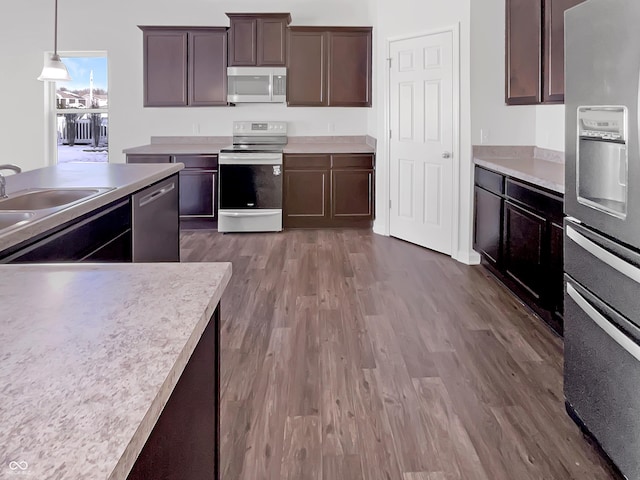 kitchen featuring dark wood finished floors, dark brown cabinetry, light countertops, appliances with stainless steel finishes, and decorative light fixtures