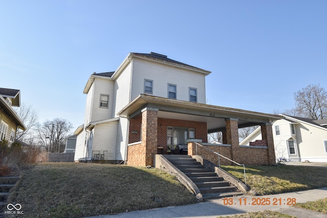 view of front facade with brick siding, covered porch, and a front lawn