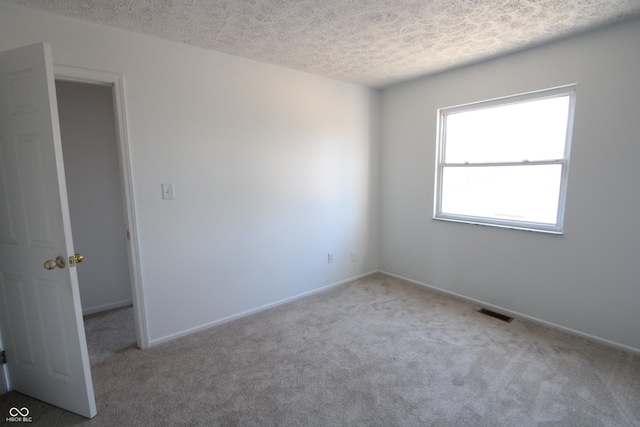 carpeted spare room featuring visible vents, a textured ceiling, and baseboards