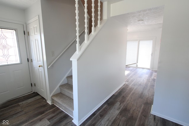 foyer with stairway, a textured ceiling, dark wood-type flooring, and baseboards