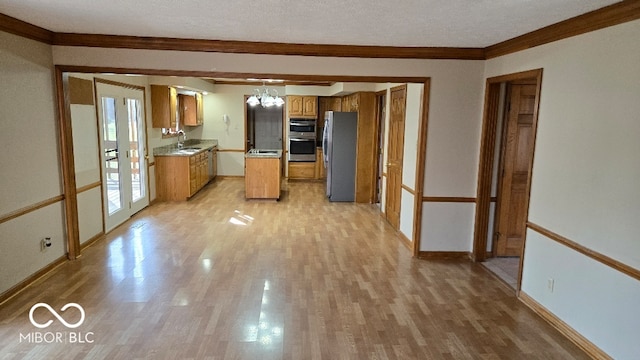 kitchen with crown molding, appliances with stainless steel finishes, an inviting chandelier, light wood-style floors, and brown cabinetry