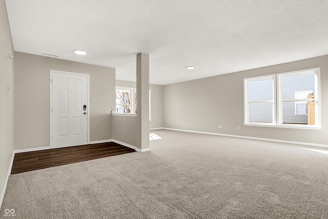 unfurnished room featuring a textured ceiling, baseboards, and dark colored carpet