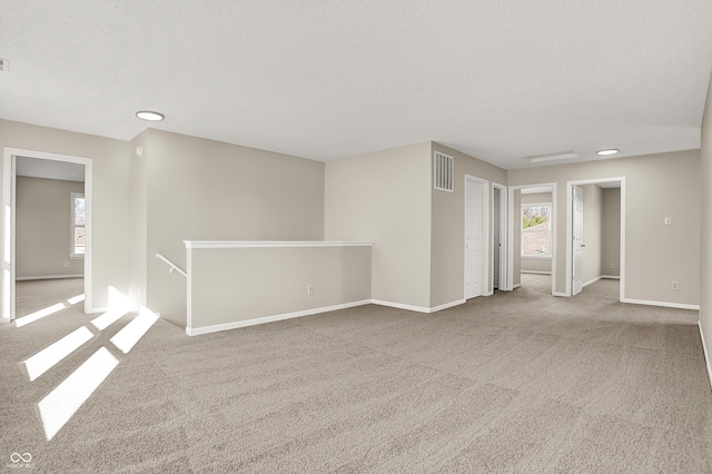 unfurnished room with a textured ceiling, carpet, visible vents, and baseboards