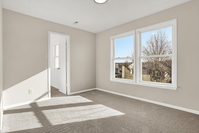 unfurnished room with carpet flooring, a textured ceiling, baseboards, and visible vents