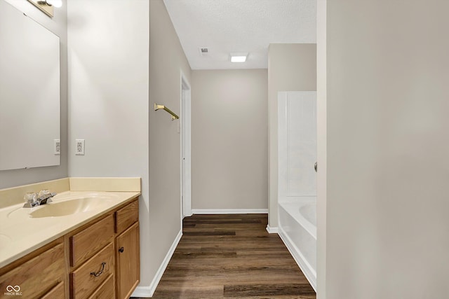 bathroom with baseboards, vanity, a bathtub, wood finished floors, and a textured ceiling