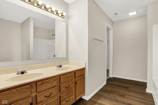 bathroom with double vanity, wood finished floors, baseboards, and a sink