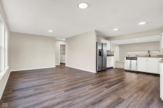 unfurnished living room with a sink, a textured ceiling, dark wood-style floors, washing machine and dryer, and baseboards