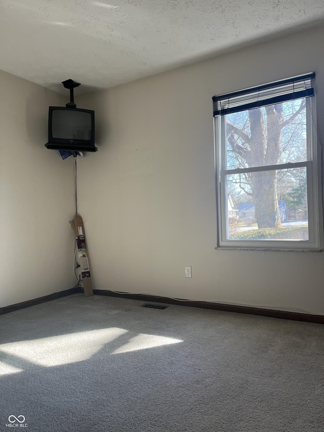 carpeted empty room with visible vents, a textured ceiling, and baseboards