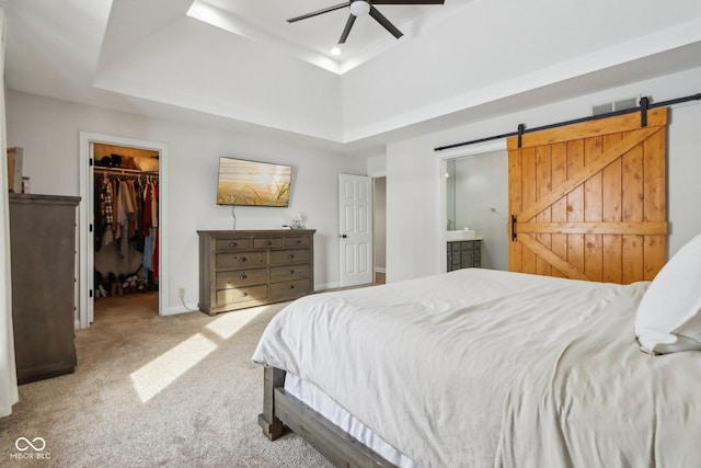 carpeted bedroom featuring a barn door, a raised ceiling, visible vents, and a walk in closet