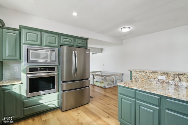 kitchen featuring appliances with stainless steel finishes, green cabinets, light wood finished floors, decorative backsplash, and light stone countertops