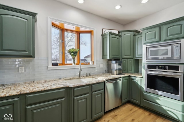 kitchen with backsplash, green cabinets, light wood-style flooring, stainless steel appliances, and a sink