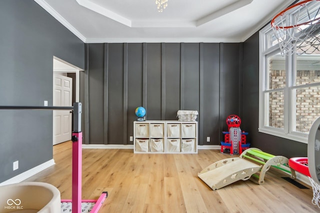 playroom with a raised ceiling, crown molding, wood finished floors, and baseboards