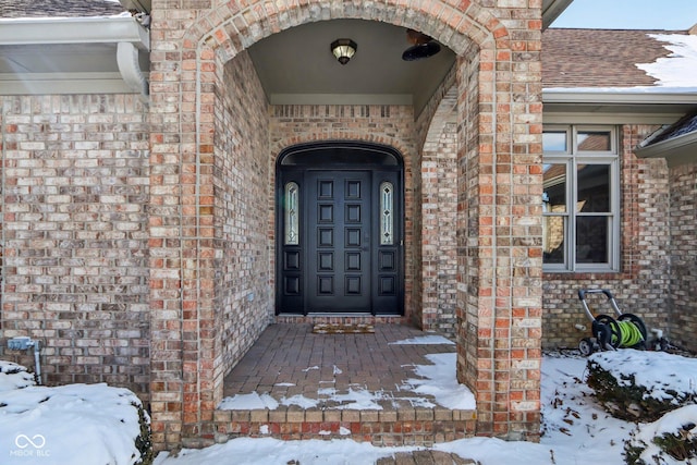 snow covered property entrance featuring brick siding and roof with shingles