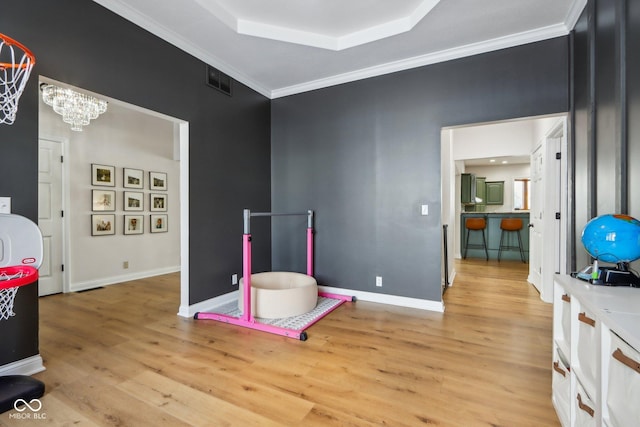 recreation room featuring crown molding, baseboards, light wood-style floors, a notable chandelier, and a raised ceiling