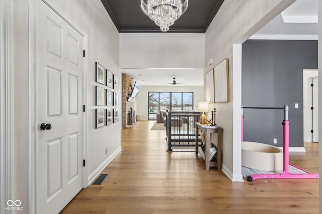 hall featuring baseboards, visible vents, light wood finished floors, an inviting chandelier, and crown molding