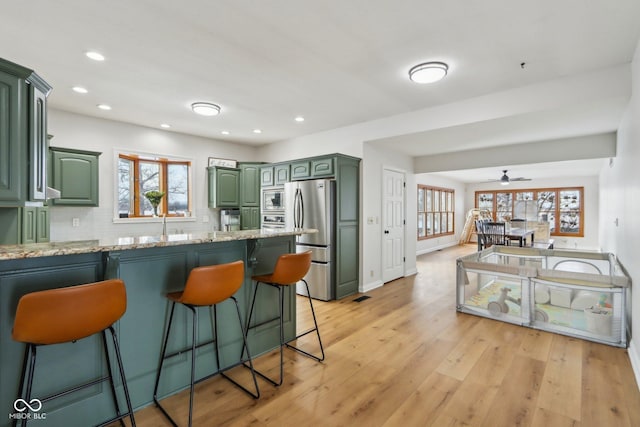 kitchen with a breakfast bar, stainless steel appliances, light wood-style floors, a peninsula, and green cabinets