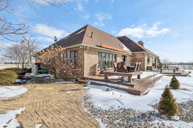 snow covered rear of property with brick siding, a deck, a chimney, and roof with shingles