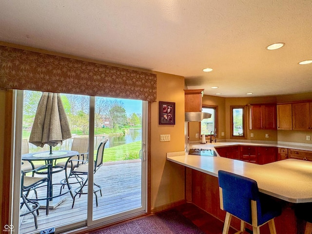 kitchen featuring black electric stovetop, light countertops, recessed lighting, a peninsula, and a water view