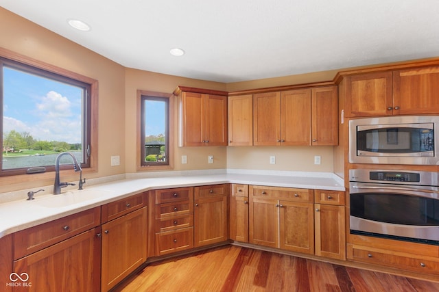 kitchen featuring brown cabinetry, light wood-style floors, light countertops, a sink, and appliances with stainless steel finishes
